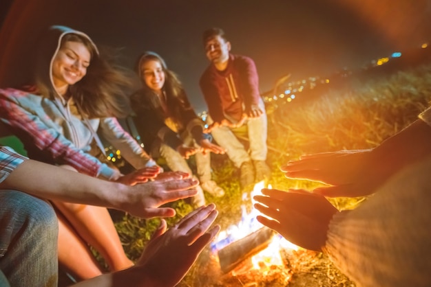 As pessoas felizes aquecendo as mãos perto de uma fogueira. noite noite