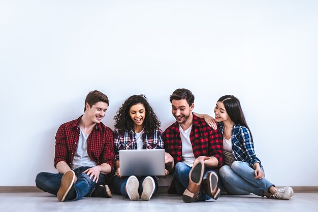 As pessoas felizes com um laptop sentado no fundo branco