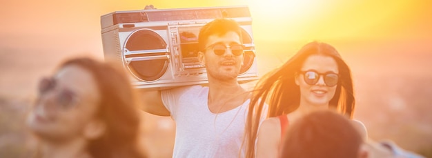 As pessoas felizes dançando com uma caixa de som no fundo do sol brilhante