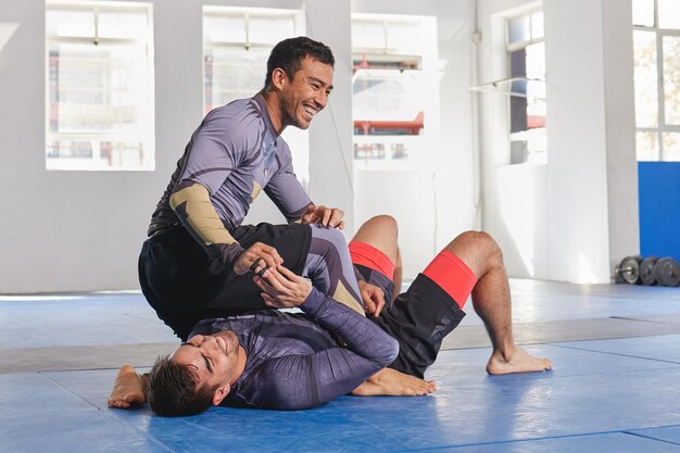 As pessoas riem juntas no ginásio de artes marciais e fitness com combate jiu jitsu e alunos aprendendo habilidades de autodefesa Exercício de luta e MMA com esporte de luta e homens com diversão e treino no dojo