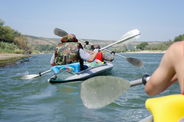 As pessoas sentam-se em caiaque e remos viagem de verão ativa em rafting na natureza