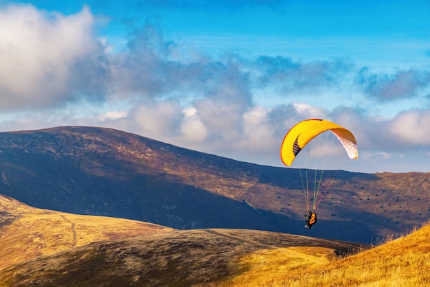 As pessoas tentam esportes de aventura de parapente voando com pára-quedas coloridos contra nuvens brancas pesadas de cumulus no céu azul no dia do outono