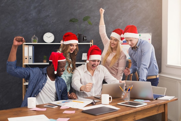 As pessoas trabalham no escritório no ano novo. equipe de negócios feliz com chapéu de papai noel, olhando para a tela do computador e sorrindo, comemorando o ano financeiro de sucesso, copie o espaço