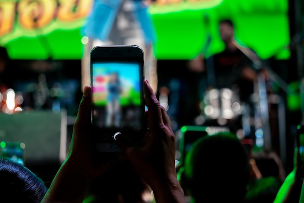 As pessoas usam telefones celulares para viver ou tirar fotos em shows, com luzes fortes à noite.