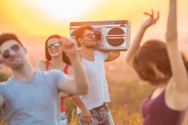 Foto as quatro pessoas com um aparelho de som dançando no fundo do pôr do sol