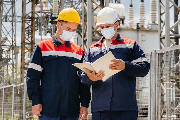 As subestações elétricas dos engenheiros realizam uma pesquisa de modernos equipamentos de alta tensão na máscara no momento da pandemia. Energia. Indústria.