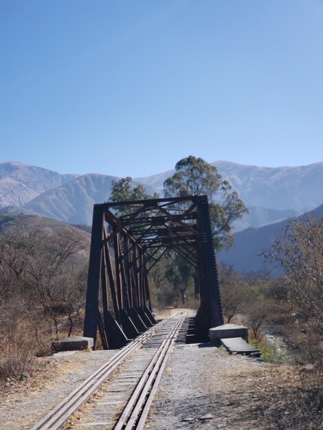 Foto as trilhas da ferrovia levam para as montanhas contra um céu claro.