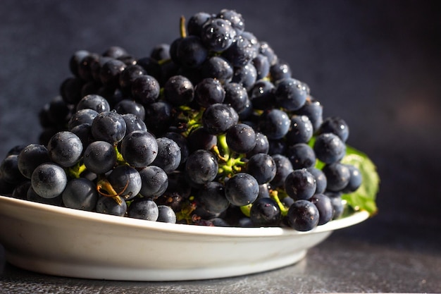 As uvas pretas estão em um prato branco com uma faixa verde oval