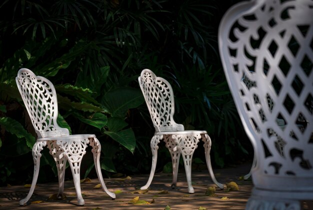 As velhas cadeiras de metal branco vintage no chão de paralelepípedos com plantas verdes na área de jardinagem