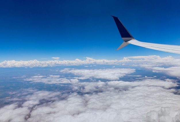 Asa de avião voando acima das nuvens no céu, vista pela janela no céu nublado, o plano de fundo da terra