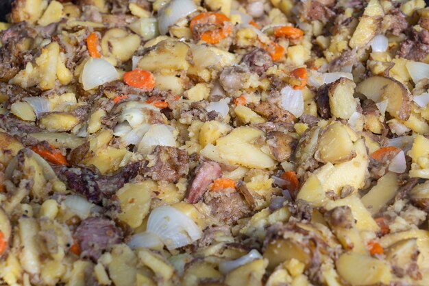 Asa las patatas, las zanahorias, las cebollas y la carne en una sartén grande. Comida deliciosa en el festival. Cocina de campo en el hogar. Las patatas jóvenes se fríen en aceite, comida callejera, Ucrania