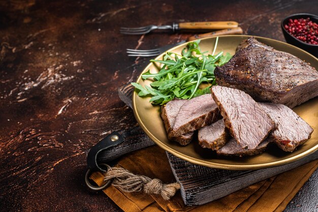 Asado Tri Tip o bistec de solomillo en un plato con rúcula Fondo oscuro Vista superior Espacio de copia