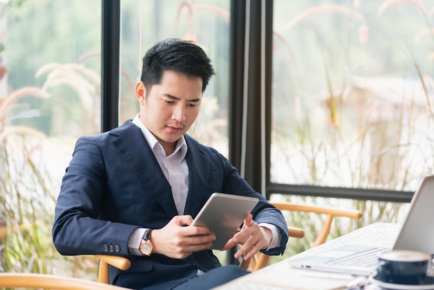 Asain empresario trabajando en tableta mientras está sentado junto a la ventana en el café