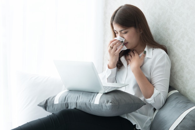 Asain mulher tem febre, Ela espirra durante o uso de laptop no quarto.