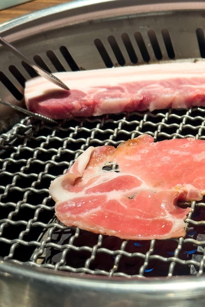 Foto asar carne de panceta de cerdo en una red redonda de barbacoa en un restaurante para comer