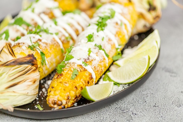 Asar elote de maíz callejero mexicano adornado con especias y cilantro fresco en un plato para servir.