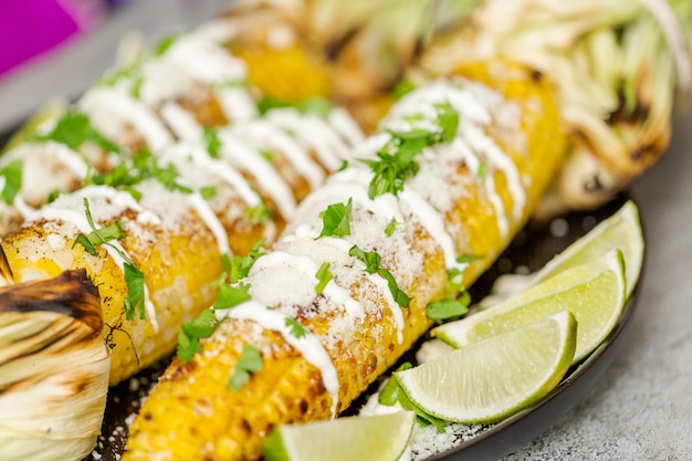 Foto asar elote de maíz callejero mexicano adornado con especias y cilantro fresco en un plato para servir.