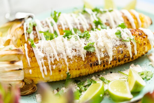 Asar elote de maíz callejero mexicano adornado con especias y cilantro fresco en un plato para servir.