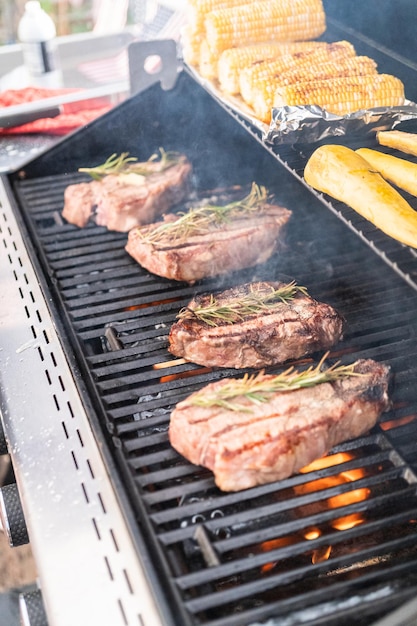 Asar un filete de Nueva York con una rodaja de mantequilla y romero en una parrilla de gas al aire libre.