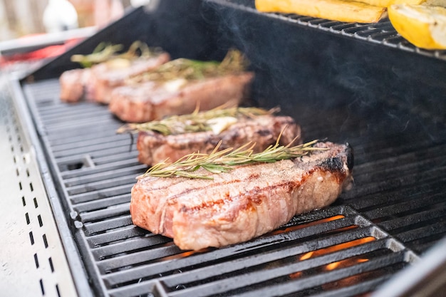 Asar un filete de Nueva York con una rodaja de mantequilla y romero en una parrilla de gas al aire libre.