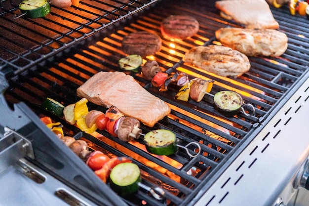 Asar salmón del Atlántico, pechuga de pollo, brochetas de verduras y hamburguesas vegetarianas en una parrilla al aire libre.