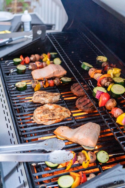 Asar salmón del Atlántico, pechuga de pollo, brochetas de verduras y hamburguesas vegetarianas en una parrilla al aire libre.