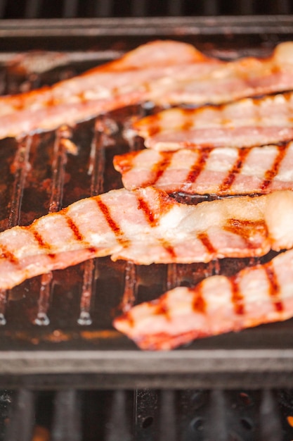 Asar tiras de tocino en una plancha de hierro fundido en una parrilla de gas al aire libre.