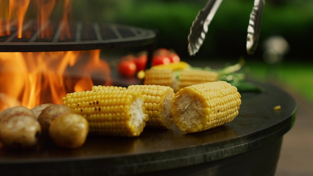 Asar verduras cocinar al fuego fuera Manos de hombre girando maíz con fórceps