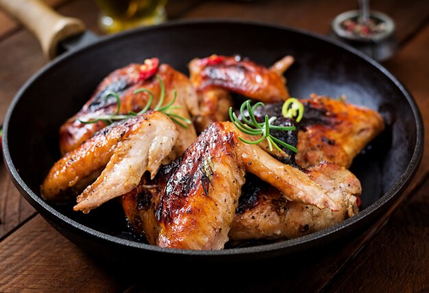 Asas de frango assadas na panela na mesa de madeira.