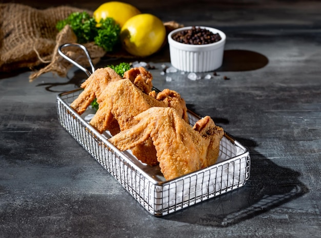 Asas de frango crocantes na fritadeira com vista superior de limão e pimenta preta em fundo escuro