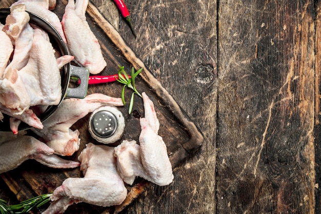 Asas de frango cru com alho e ervas em uma tigela. Em fundo de madeira.