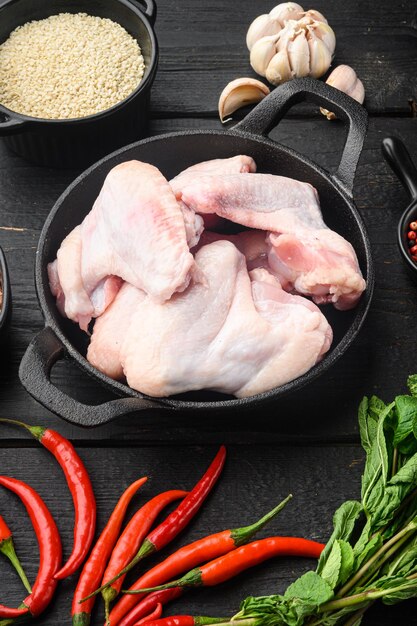 Asas de frango cru com ervas e gergelim em frigideira de ferro fundido na mesa de madeira preta