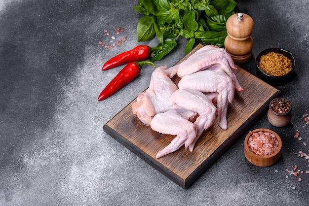 Asas de frango cru com ingredientes para cozinhar em uma tábua de madeira