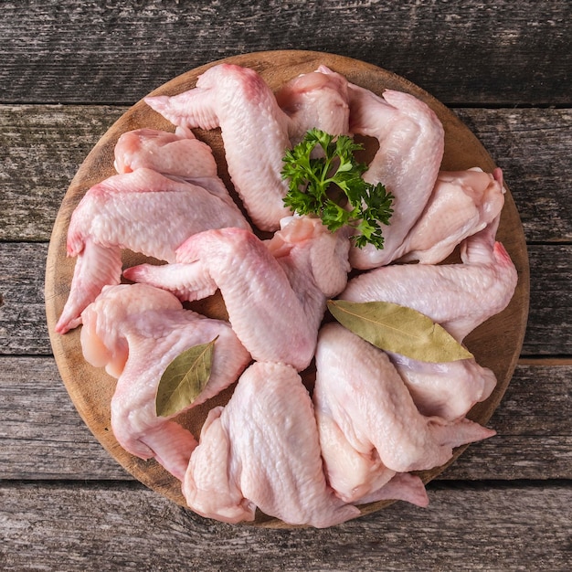 Asas de frango cru com ingredientes para cozinhar na placa de madeira. Vista do topo