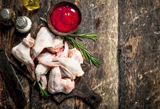 Asas de frango cru com molho de tomate e ervas. Em uma mesa de madeira.