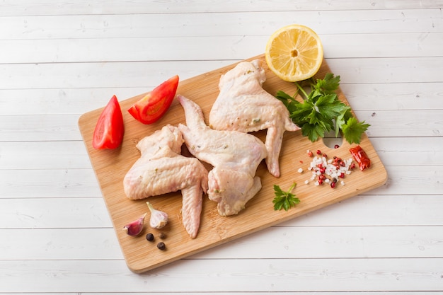 Asas de frango cru com pimenta e verduras no carrinho de madeira