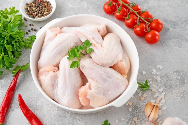 Asas de frango cru em um prato branco com especiarias de ervas frescas para cozinhar Espaço de cópia de vista superior