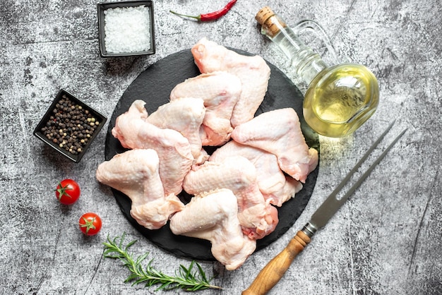 Asas de frango cru em um prato preto com azeite, tomate, azeite e limão