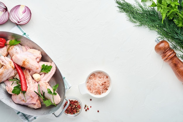 Asas de frango cru em uma tigela branca com temperos e ingredientes para cozinhar em superfície de concreto leve