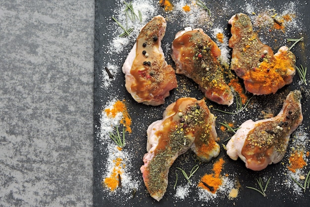 Asas de frango cru marinado em especiarias em uma placa de pedra preta.