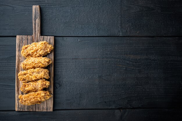 Asas de frango empanadas fritas picantes cortam em madeira preta