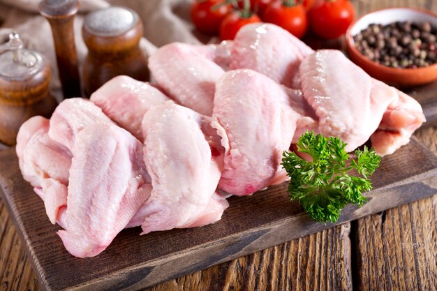 Asas de frango frescas com ingredientes para cozinhar na tábua de madeira