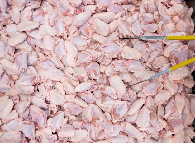 Foto asas de frango frescas no meio da bandeja de metal com pinças de alimentos para venda no produto de mercado da fazenda orgânica acima vista com o espaço de cópia