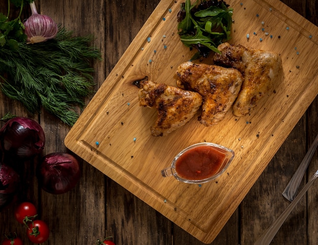 Asas de frango frito decoradas com vegetais em uma bandeja de madeira, vista superior