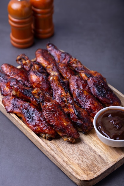 Asas de frango frito em uma placa de madeira com molho de churrasco.