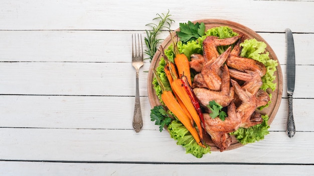 Asas de frango grelhadas com legumes e cenouras em um fundo de madeira vista superior Copiar espaço