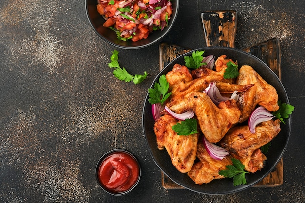 Asas de frango grelhadas ou churrasco assado com especiarias e molho de tomate em uma placa preta. Vista superior com espaço de cópia.