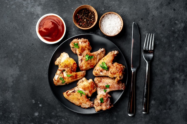 asas de frango grelhado em molho de churrasco com salsa em um prato preto sobre uma mesa de concreto.