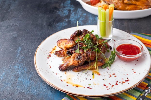 Asas de frango para churrasco servidas com legumes e ketchup em um prato Copiar espaço