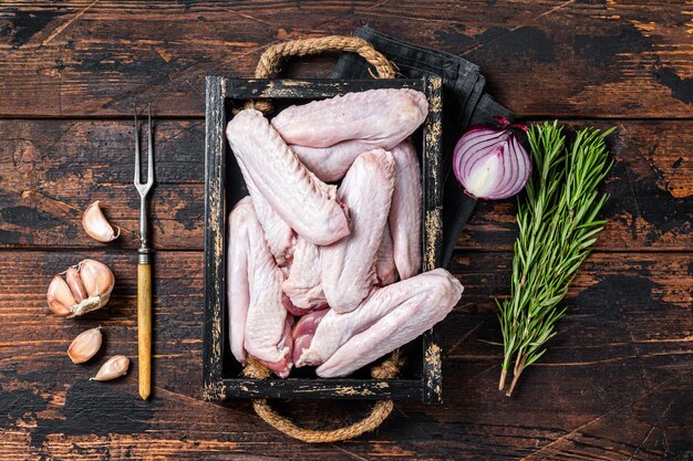 Asas de pato e frango cru fresco em uma bandeja. Fundo de madeira escuro. Vista do topo.